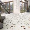 Bright contemporary lobby with terrazzo-style floor, a glass staircase, seating area, and large floor-to-ceiling windows letting in sunlight.